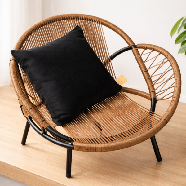 Sillón de rattan moderno con estructura metálica negra y almohadón negro sobre superficie de madera clara